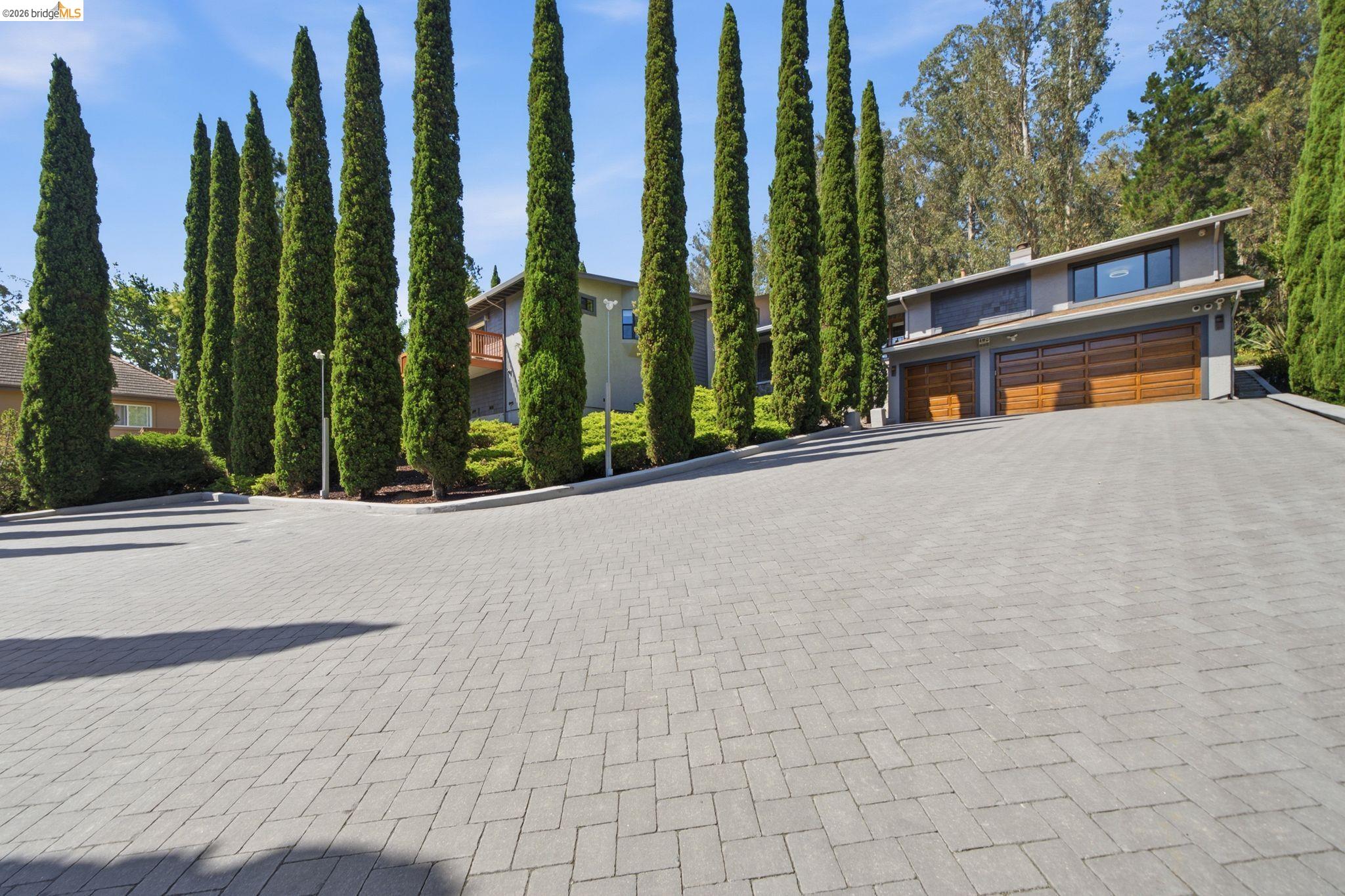 11133 Golf Links Road Oakland, CA 94605 - Photo 1 of 57 Paver stone driveway leading to a residence featuring a modern exterior, wood-finish garage doors, and an upper-level window bank