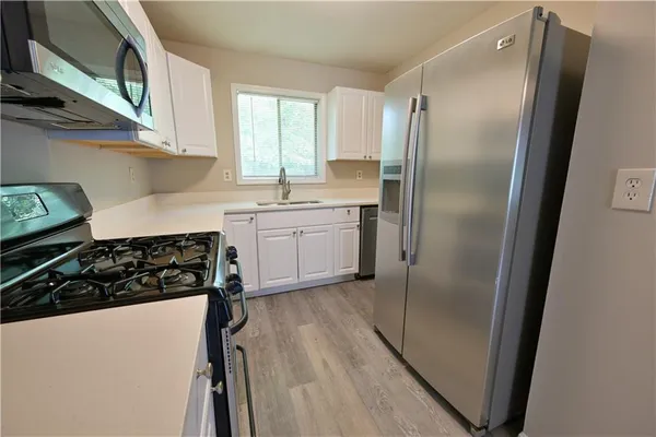 a kitchen with stainless steel appliances granite countertop a refrigerator a sink a stove and white cabinets with wooden floor