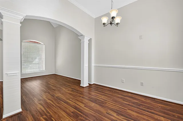 an empty room with wooden floor chandelier fan and windows