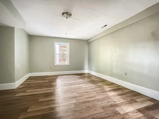 a view of an empty room with window and wooden floor