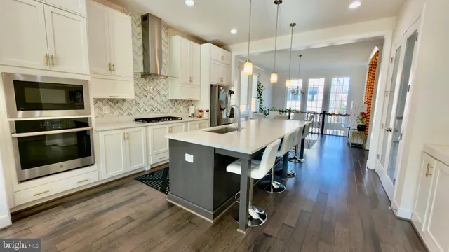 a kitchen with stainless steel appliances a stove a sink a microwave a refrigerator and white cabinets with wooden floor