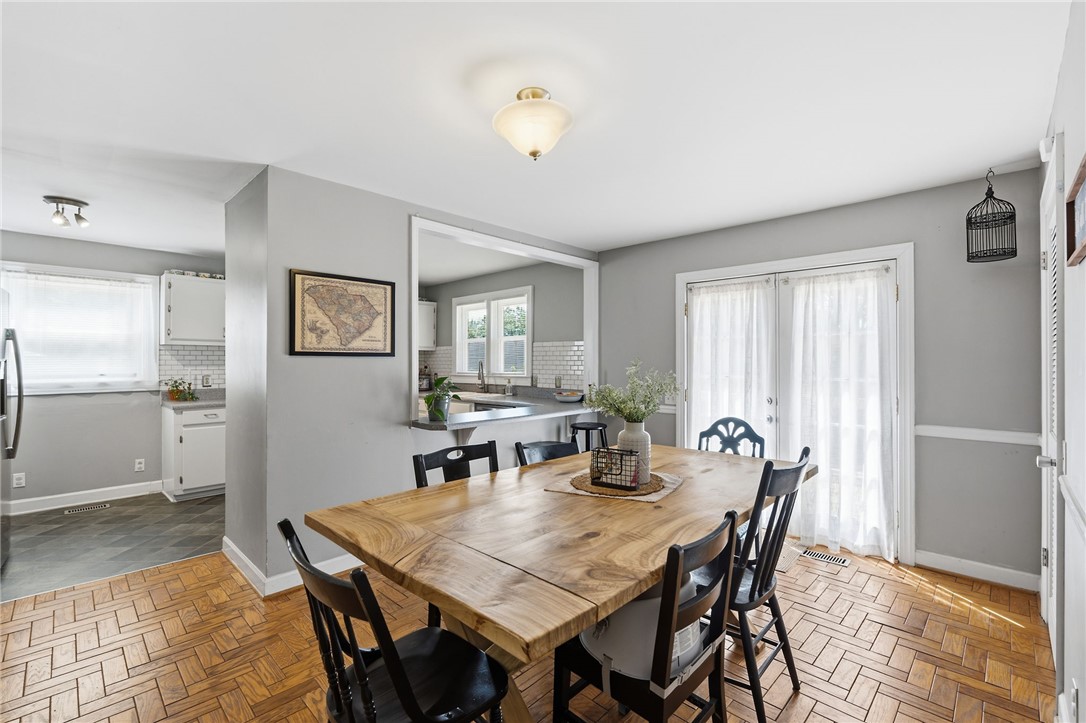 108 Tarrant Street Central, SC 29630 - Photo 12 of 42 Herringbone wood flooring defines the dining space, flowing seamlessly to a pass-through kitchen with white cabinetry and subway tile.