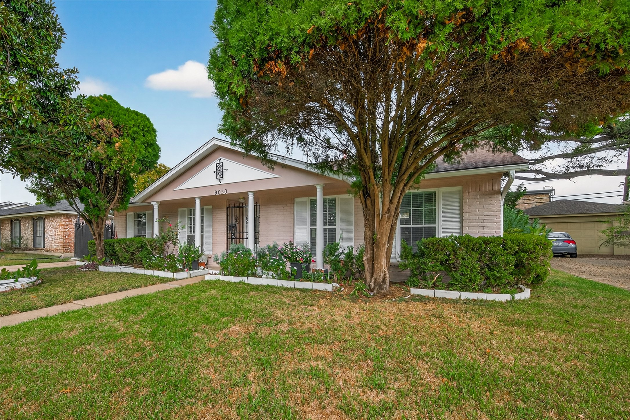 9030 Troulon Drive Houston, TX 77036 - Photo 34 of 34 Angled perspective of the home's front, featuring well-maintained flower beds, classic white shutters, and a welcoming covered porch entrance.