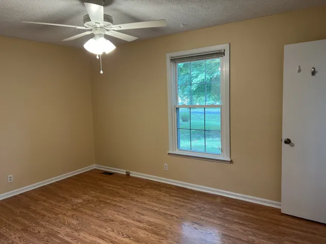 an empty room with wooden floor fan and windows