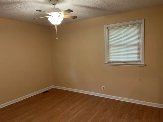 a view of an empty room with a window and wooden floor