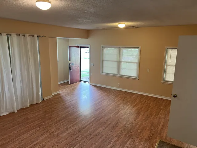 a view of an empty room with wooden floor and a window