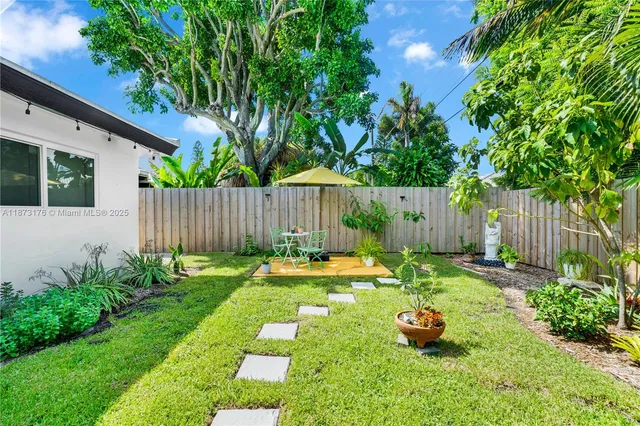 a backyard of a house with table and chairs plants and large tree