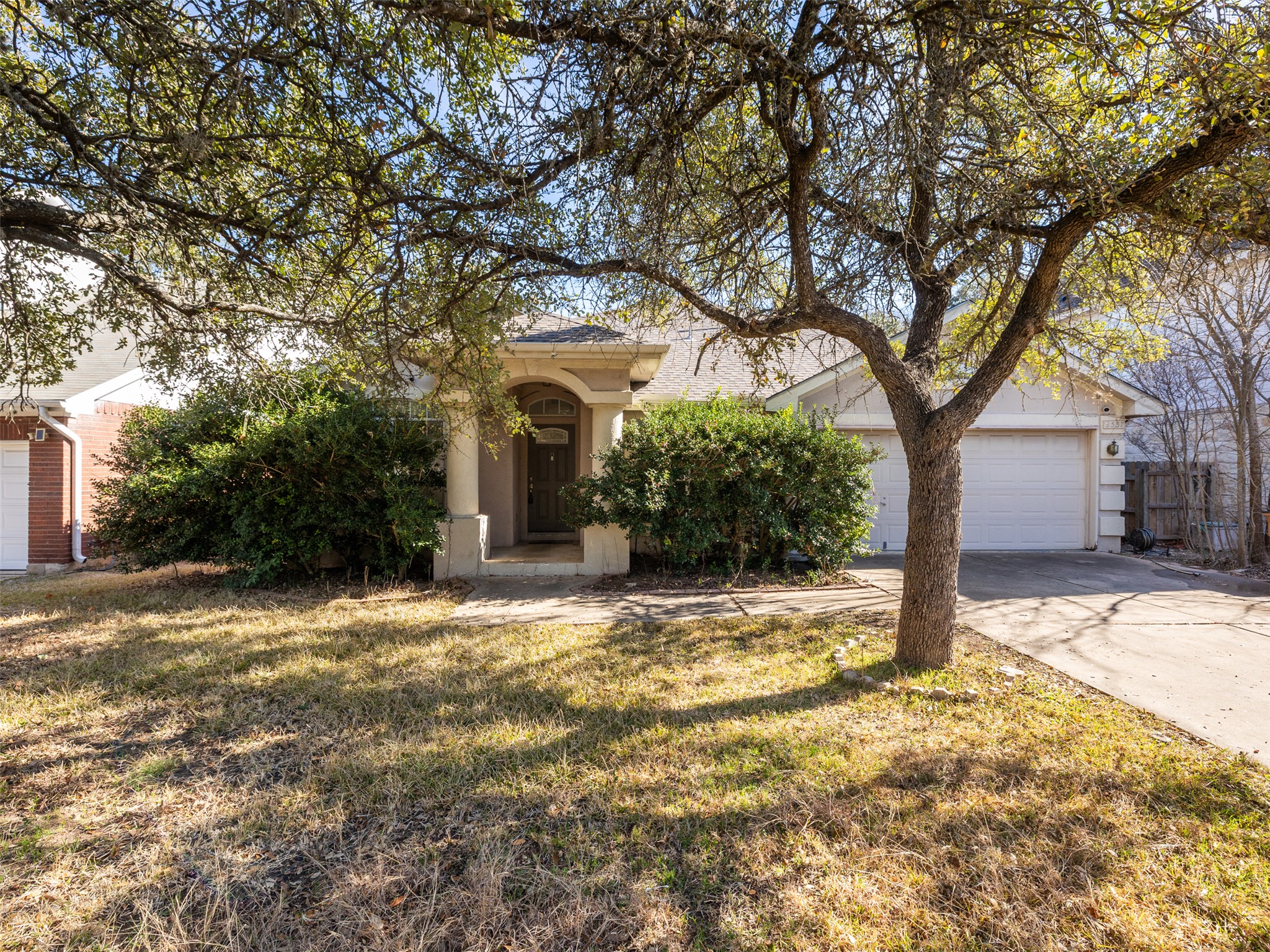 View of property hidden behind natural elements featuring driveway, a front yard, and a garage