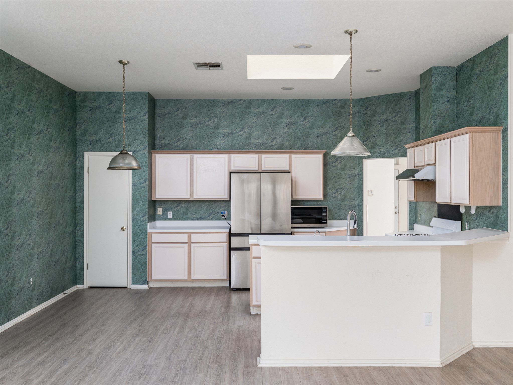 8537 Foxhound Trail Austin, TX 78729 - Photo 12 of 26 Kitchen with light countertops, a skylight, stainless steel appliances, pendant lighting, and light wood finished floors
