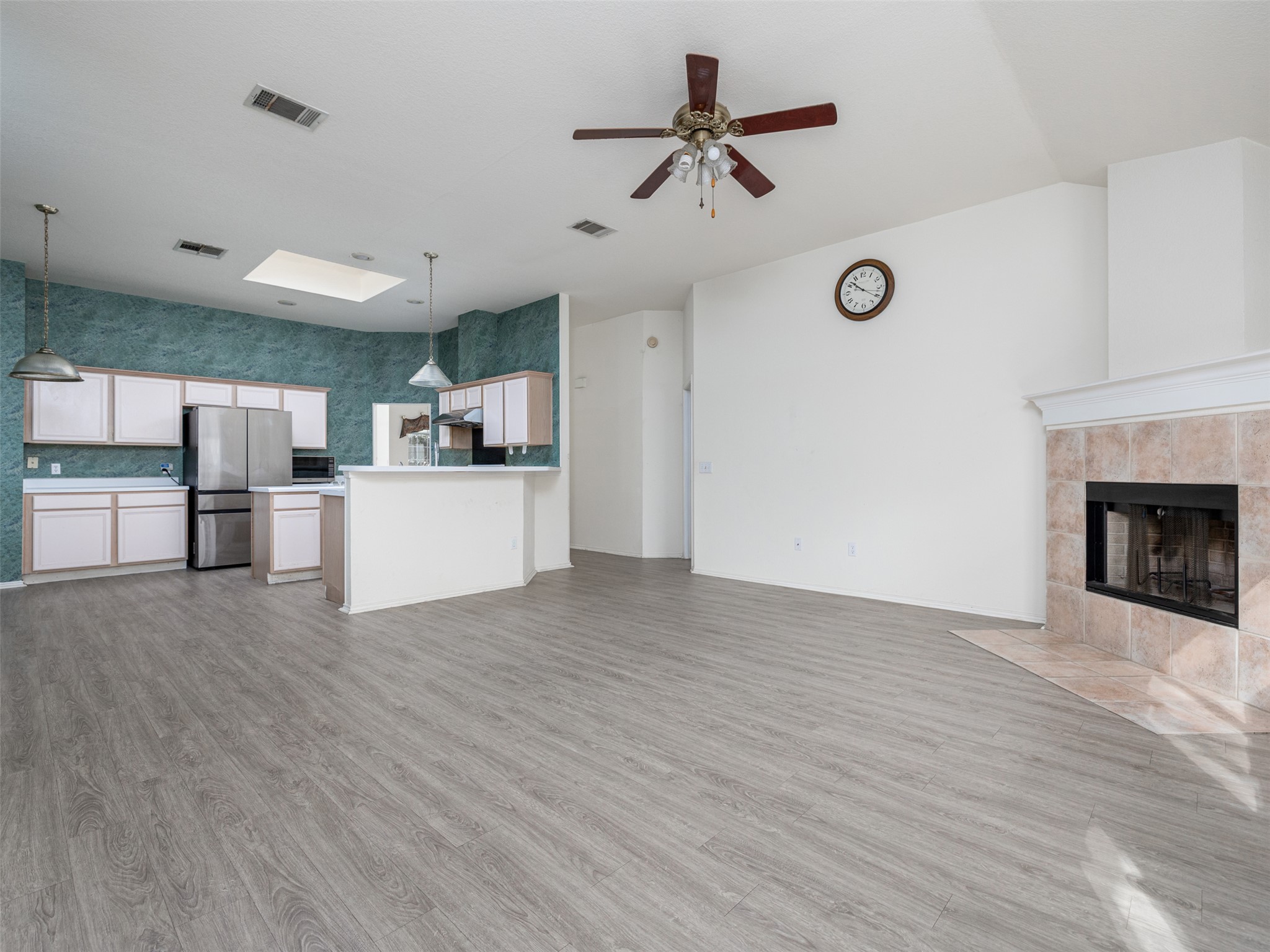 8537 Foxhound Trail Austin, TX 78729 - Photo 13 of 26 Unfurnished living room featuring light wood-style floors, a ceiling fan, a tiled fireplace, and wallpapered walls