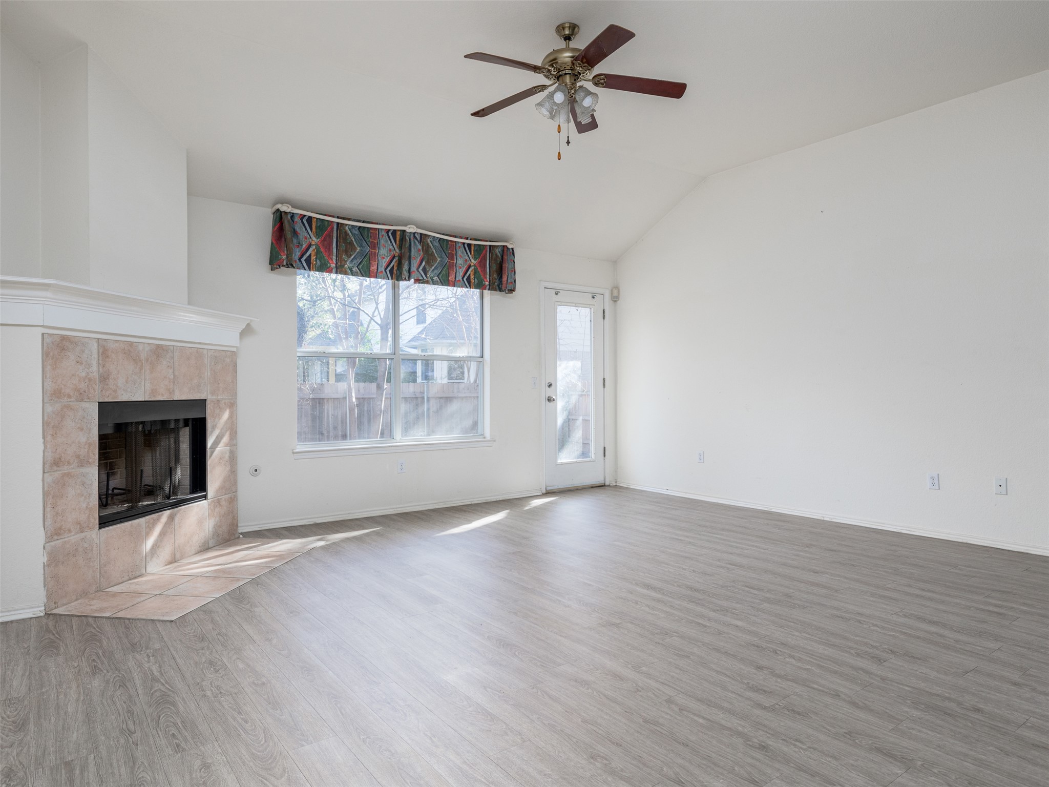 8537 Foxhound Trail Austin, TX 78729 - Photo 14 of 26 Unfurnished living room featuring ceiling fan, wood finished floors, a fireplace, and lofted ceiling