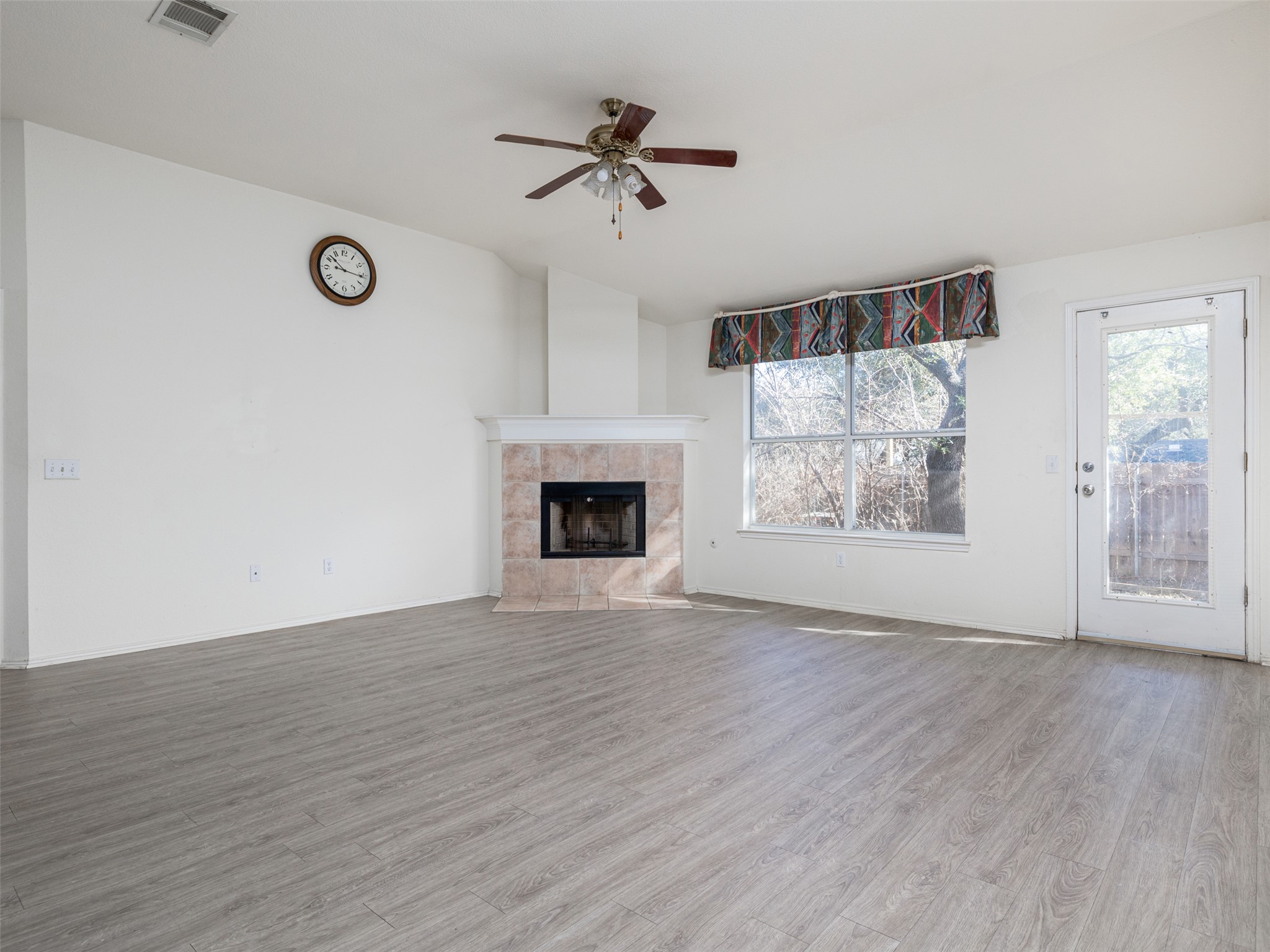 8537 Foxhound Trail Austin, TX 78729 - Photo 15 of 26 Unfurnished living room featuring a ceiling fan, light wood-style floors, vaulted ceiling, and a fireplace