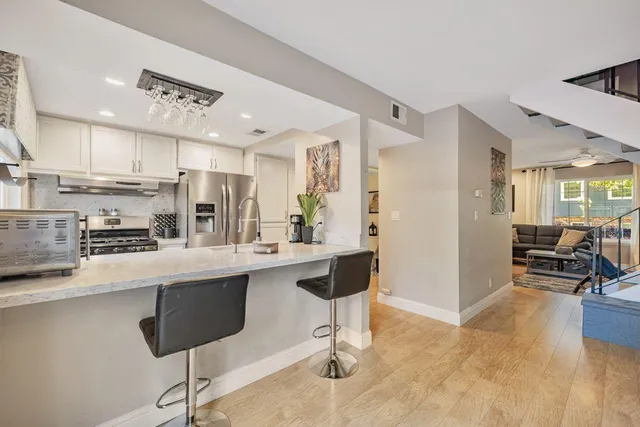 a kitchen with stainless steel appliances kitchen island granite countertop a refrigerator a stove a sink and a dining table with wooden floor