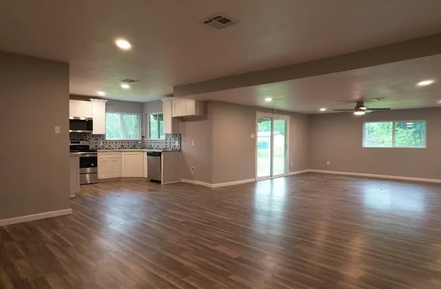 an empty room with wooden floor kitchen view and windows