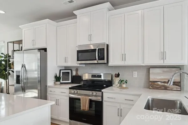 a kitchen with stainless steel appliances granite countertop a refrigerator a stove a sink and white cabinets