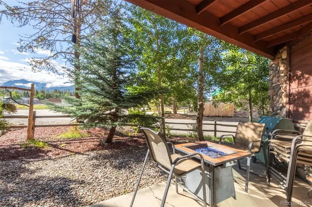 a view of patio with table and chairs and couches with wooden fence and large trees