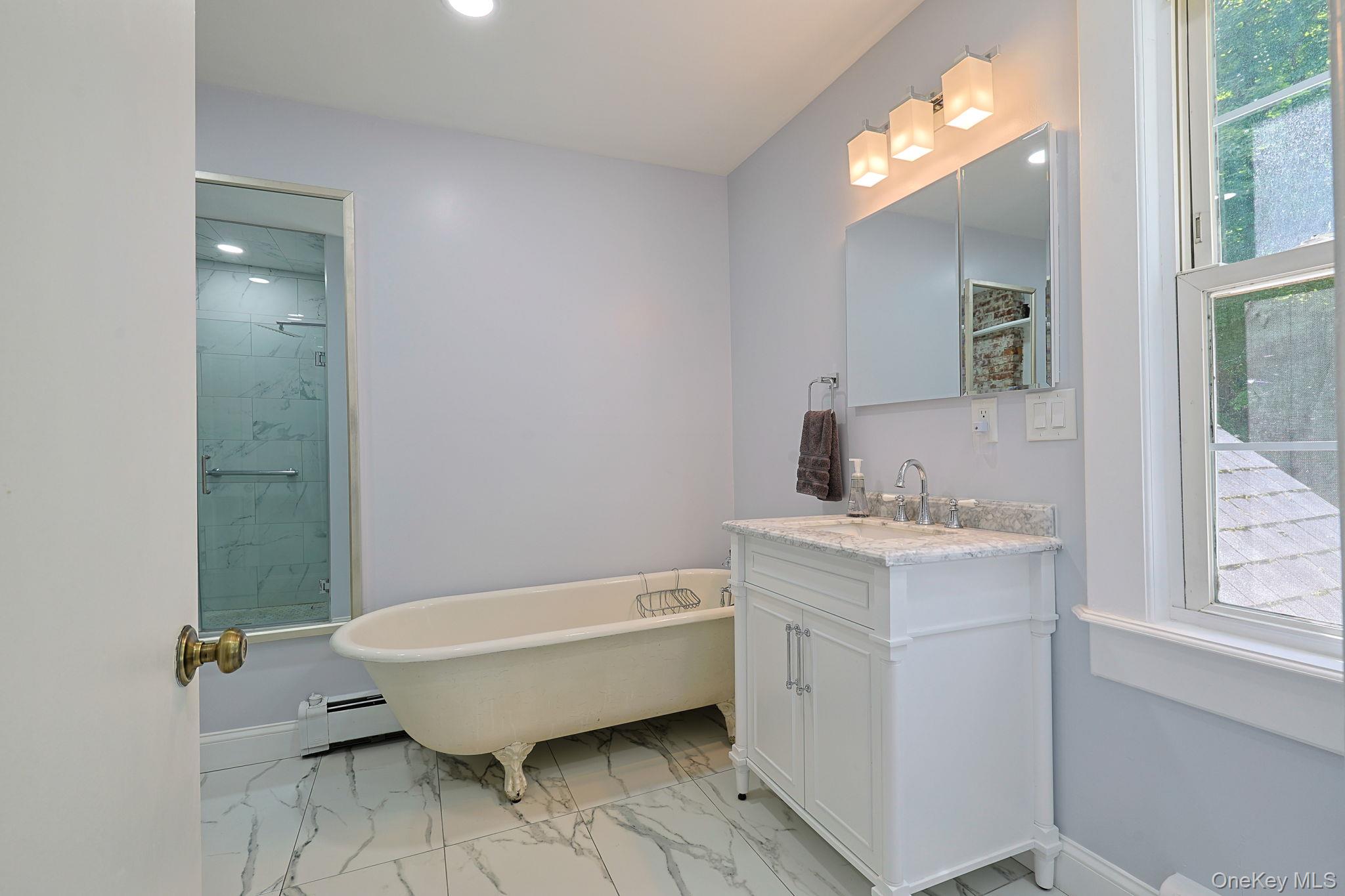 9 Library Road Tuxedo Park, NY 10987 - Photo 15 of 37 Bathroom featuring a freestanding clawfoot tub, a white vanity with a light-toned countertop, a mirrored medicine cabinet, a glass-enclosed shower with marble-look tile, and white marble-look floor tile