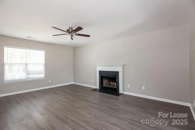 an empty room with wooden floor a ceiling fan a fireplace and windows