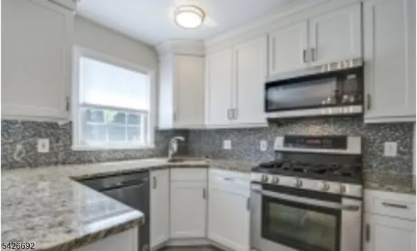 a kitchen with granite countertop white cabinets stainless steel appliances and a window