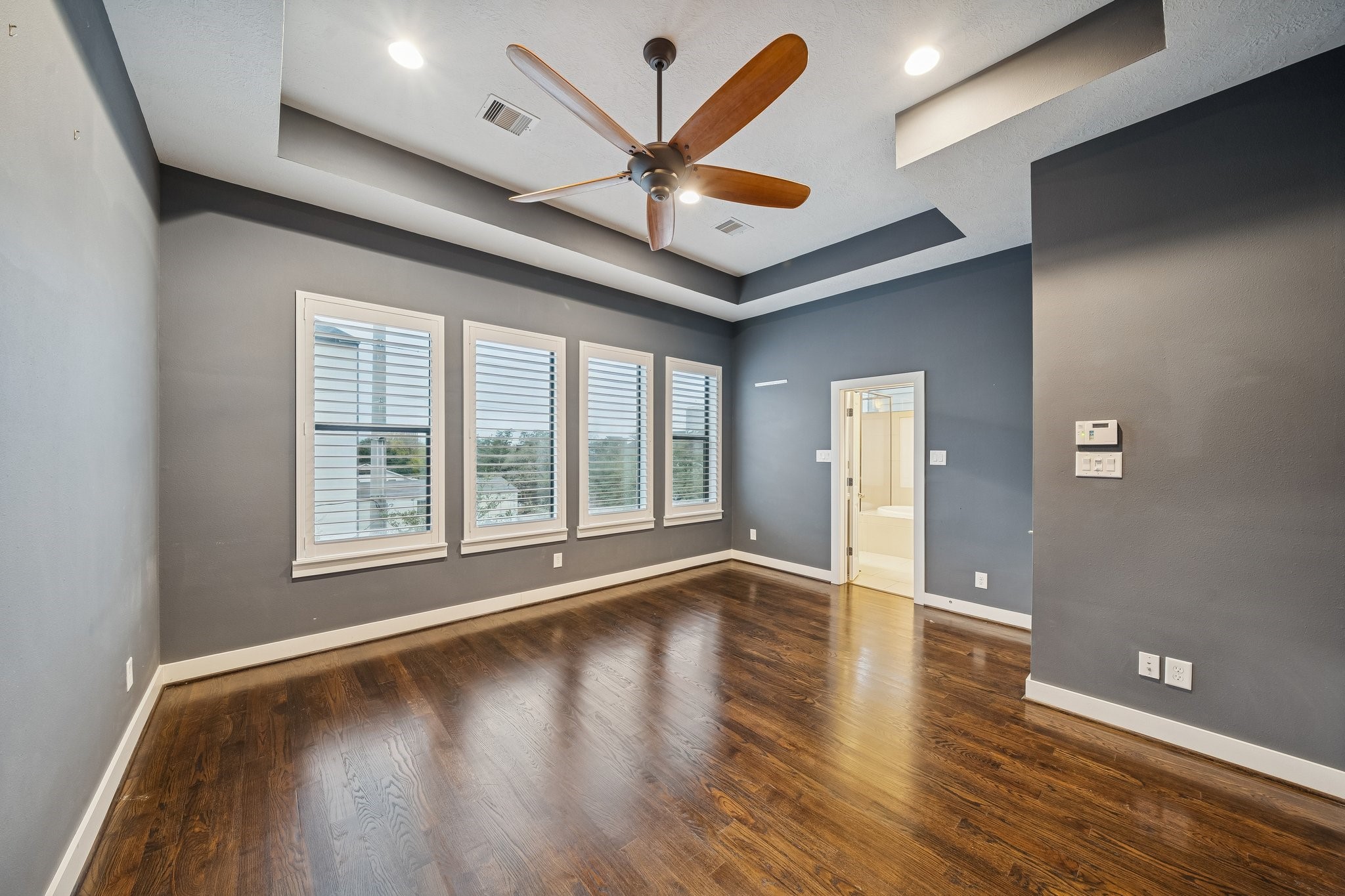 2105 Mason Street Houston, TX 77006 - Photo 11 of 43 Spacious primary bedroom featuring rich hardwoods, a tray ceiling with recessed lighting, and a ceiling fan for everyday comfort. The deep, modern wall color adds contrast and warmth, while the layout leaves plenty of room to create a true retreat with seating or a workspace.