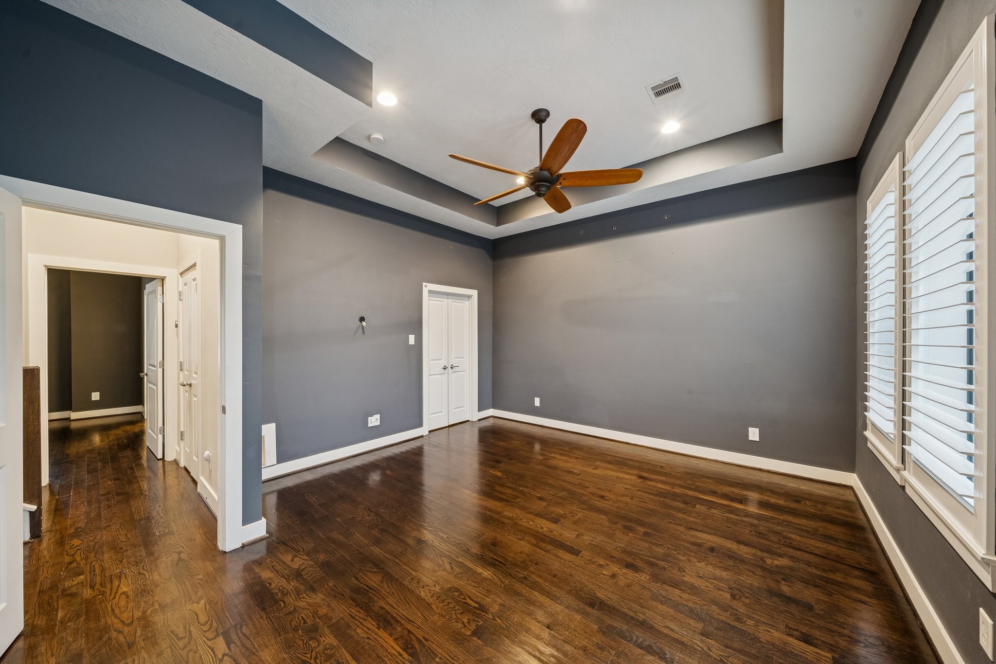 2105 Mason Street Houston, TX 77006 - Photo 12 of 43 Primary suite with a wall of windows and plantation shutters, bringing in great natural light without sacrificing privacy. Finished with hardwood floors, a tray ceiling, recessed lighting, and a ceiling fan, plus direct access to the en-suite bath for an easy, suite-style flow.
