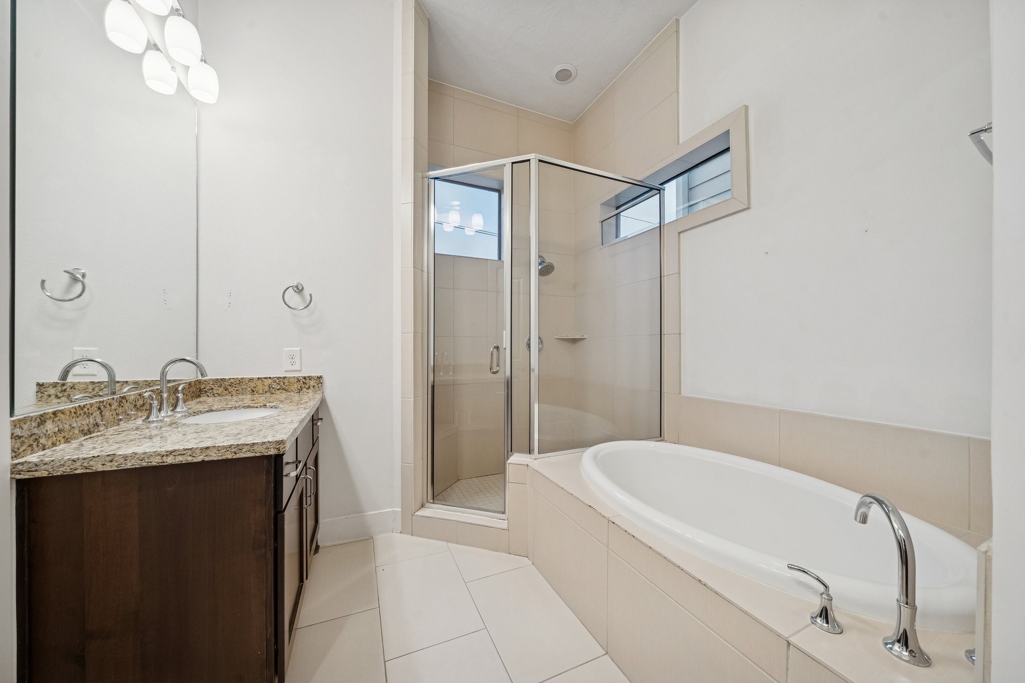 2105 Mason Street Houston, TX 77006 - Photo 14 of 43 In the primary bath, a soaking tub sits alongside a glass-enclosed shower with tiled surround and a high window for natural light. The vanity features a granite countertop, an undermount sink, and modern fixtures, paired with light tile flooring. Having both tub and separate shower gives you options depending on the day.