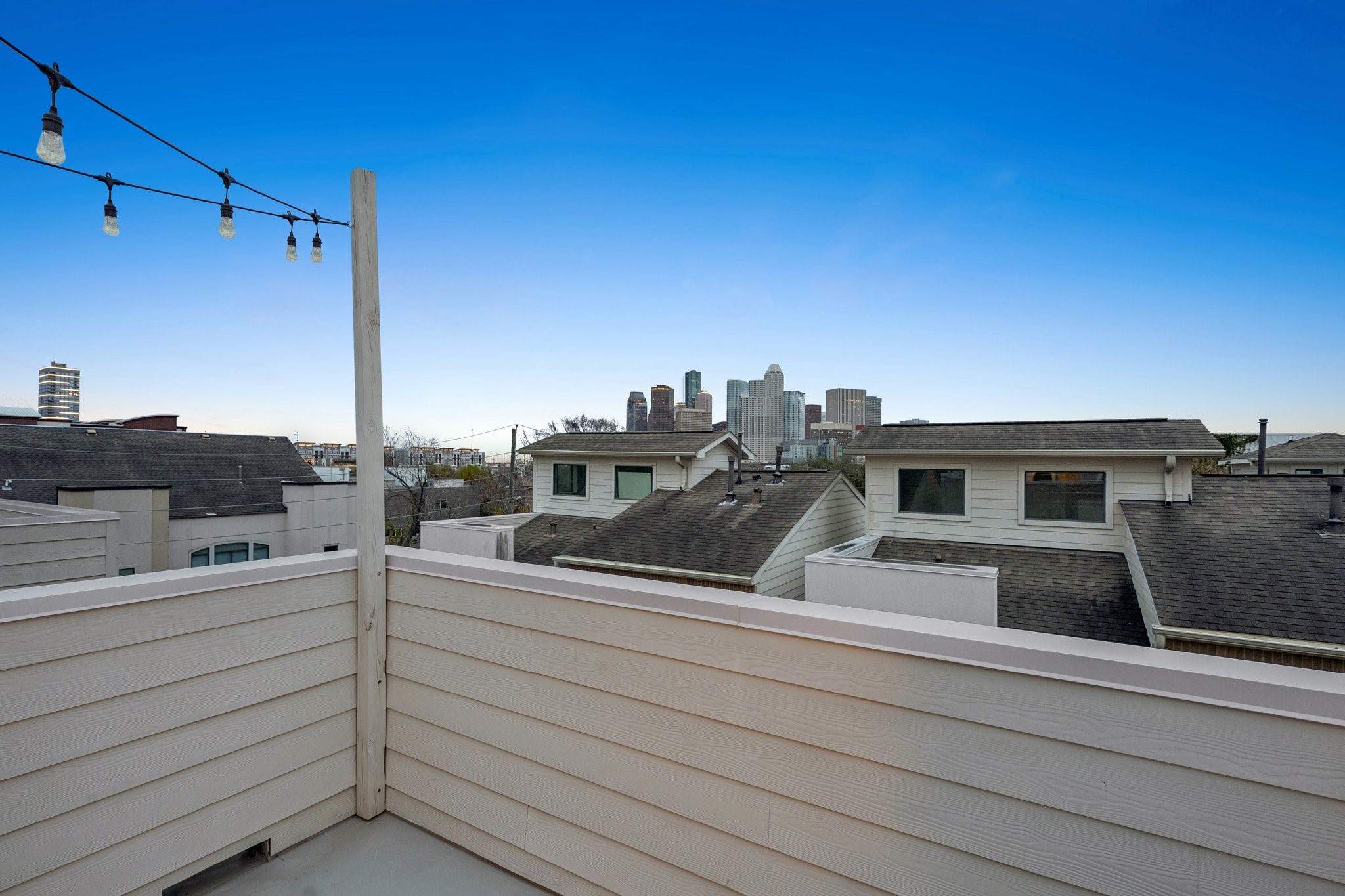 2105 Mason Street Houston, TX 77006 - Photo 17 of 43 Skyline views take center stage from this fourth-floor terrace, where the corner layout frames downtown above the surrounding rooftops. Tall privacy walls define the space without blocking the horizon line, and the string lighting overhead adds an easy setup for evening use. The open sightline makes it a natural spot for a bistro table, lounge chairs, or a simple outdoor work break.