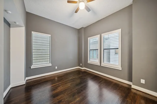 an empty room with wooden floor chandelier fan and windows