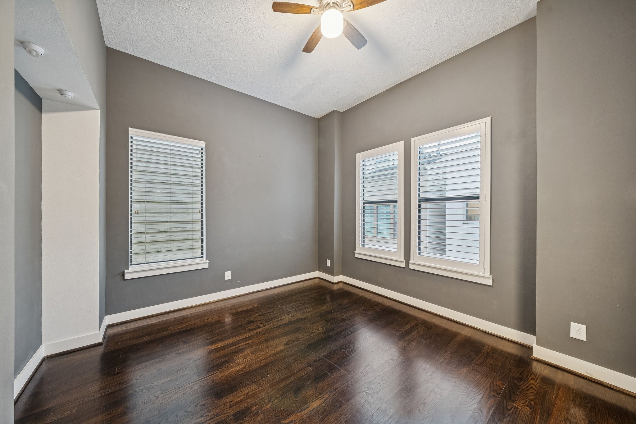 2105 Mason Street Houston, TX 77006 - Photo 23 of 43 Natural light comes in from multiple windows in this secondary bedroom, and the dark hardwood floors add a clean contrast to the gray walls and white trim. A ceiling fan with light keeps the room comfortable and bright. With windows on two sides, the space feels airy while still offering privacy.