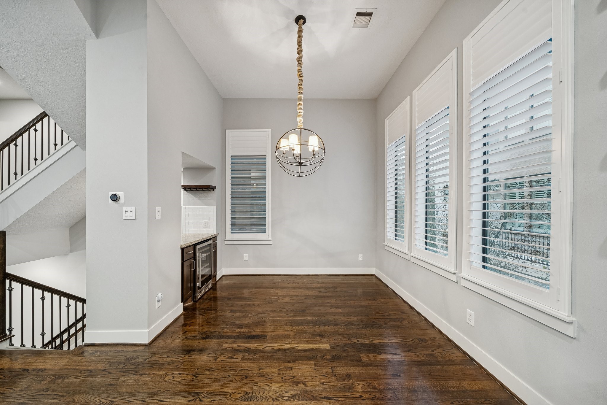 2105 Mason Street Houston, TX 77006 - Photo 31 of 43 Tucked just off the kitchen, the dining area is lined with tall windows and plantation shutters that bring in great light while keeping the look clean and finished. Dark hardwood floors and a statement pendant fixture give the space a defined feel without closing it off from the rest of the main level. The nearby built-in counter with an undercounter beverage cooler adds an easy spot for serving and everyday convenience.
