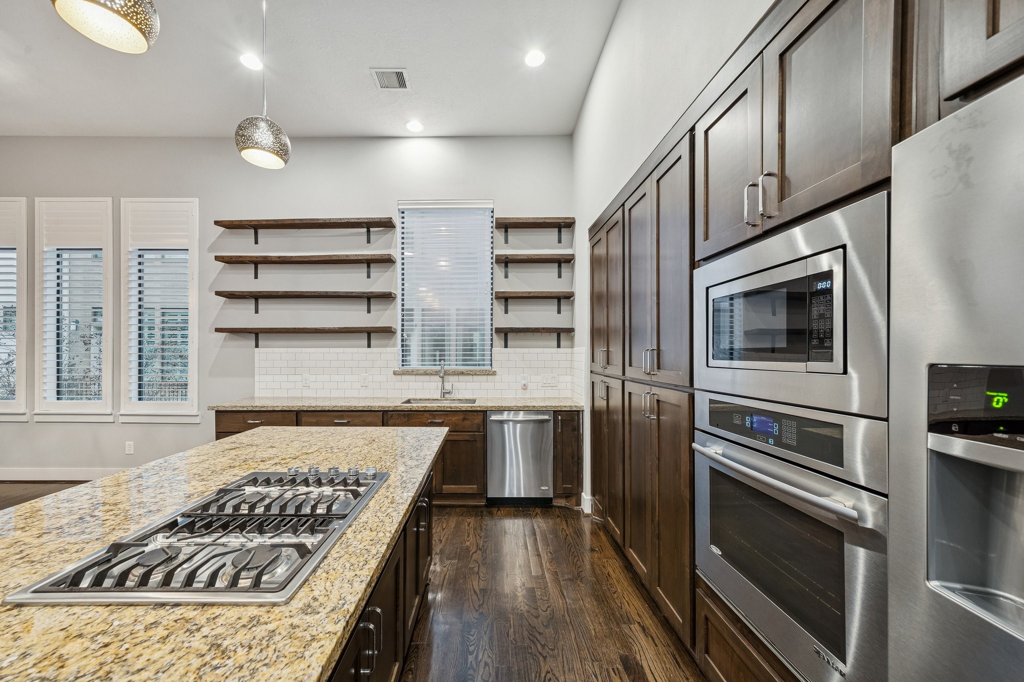 2105 Mason Street Houston, TX 77006 - Photo 32 of 43 A closer look shows the stainless built-in microwave and oven stacked into the cabinetry for a clean, integrated feel. The island cooktop keeps the cooking surface front-and-center, while the sink wall stays dedicated to prep and cleanup. Open shelving adds a practical touch for display and quick access.