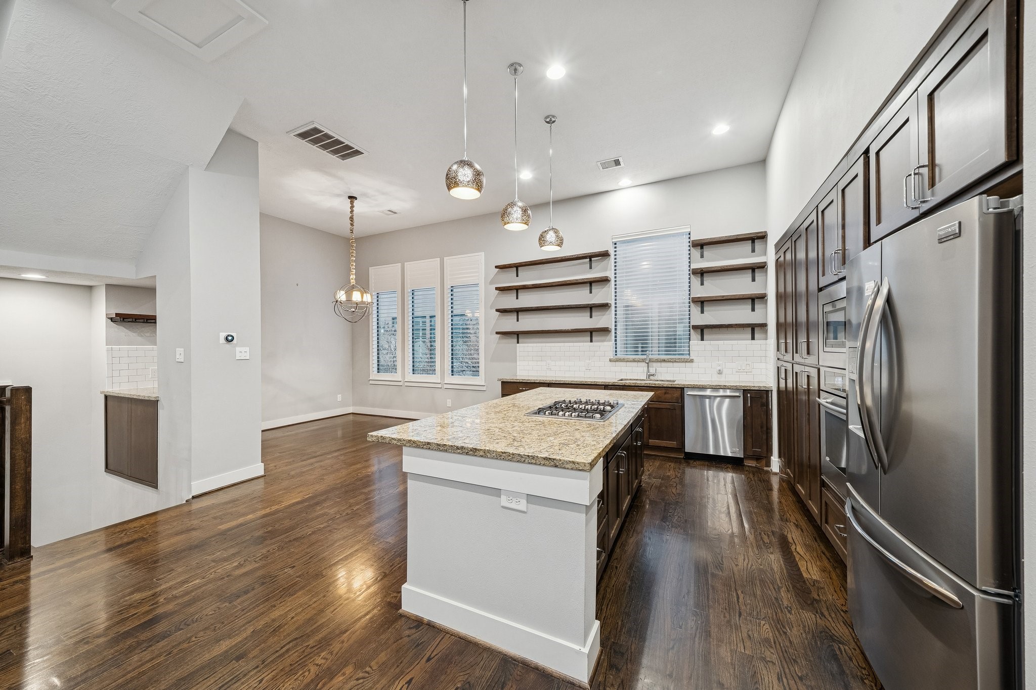 2105 Mason Street Houston, TX 77006 - Photo 33 of 43 Looking in from the side, you can see how the tall cabinet run anchors the room and frames the stainless refrigerator and built-ins. The island’s granite top and pendant lighting add contrast against the light walls. With clear space between counters and island, the kitchen stays comfortable even with multiple people moving around.