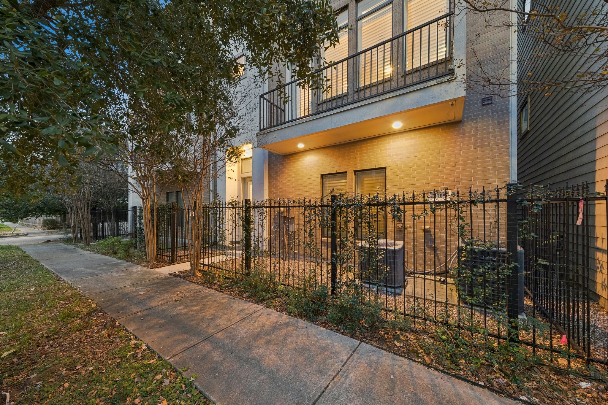 2105 Mason Street Houston, TX 77006 - Photo 38 of 43 Tucked behind a private fence on a tree-lined street, the front entry offers a quiet, welcoming approach with warm evening lighting and an easy sense of privacy. The gated walk-up sets the tone for a lock-and-leave lifestyle while still feeling inviting.