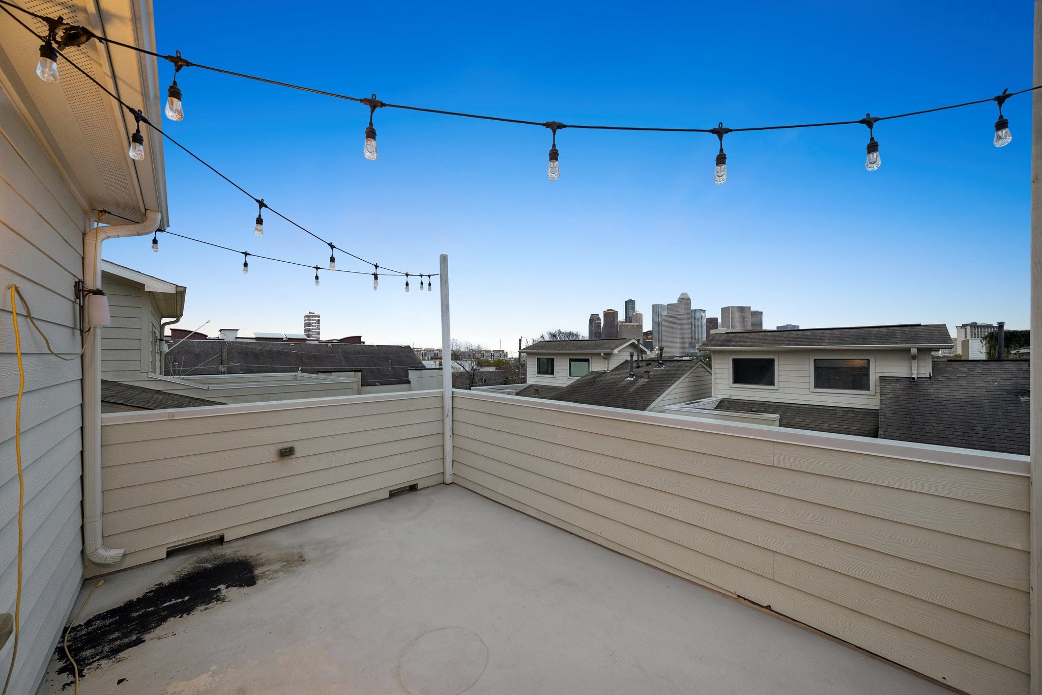 2105 Mason Street Houston, TX 77006 - Photo 42 of 43 Set high above the rooftops, this fourth-floor terrace offers an open concrete deck framed by privacy walls and overhead string lighting. The sightline toward the skyline gives the space a clear focal point, while the open layout allows space for multiple seating areas for everyday use.