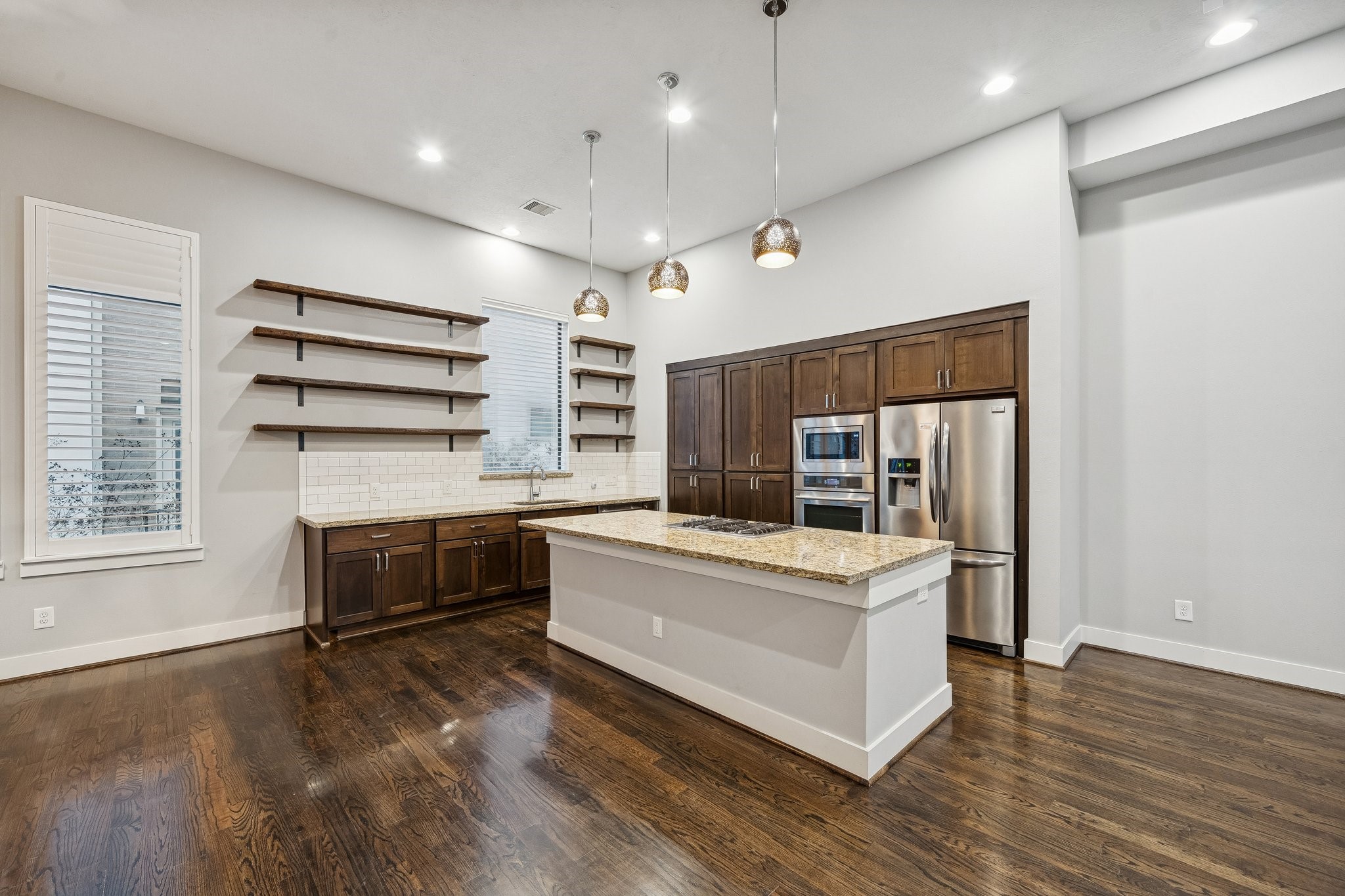 2105 Mason Street Houston, TX 77006 - Photo 6 of 43 Three pendant lights draw your eye straight to the island and give the kitchen a strong focal point. The island is topped with a speckled stone surface and includes a built-in cooktop, keeping prep and cooking centered. Along the back wall, tall cabinetry and stainless appliances keep storage and function neatly in one place.