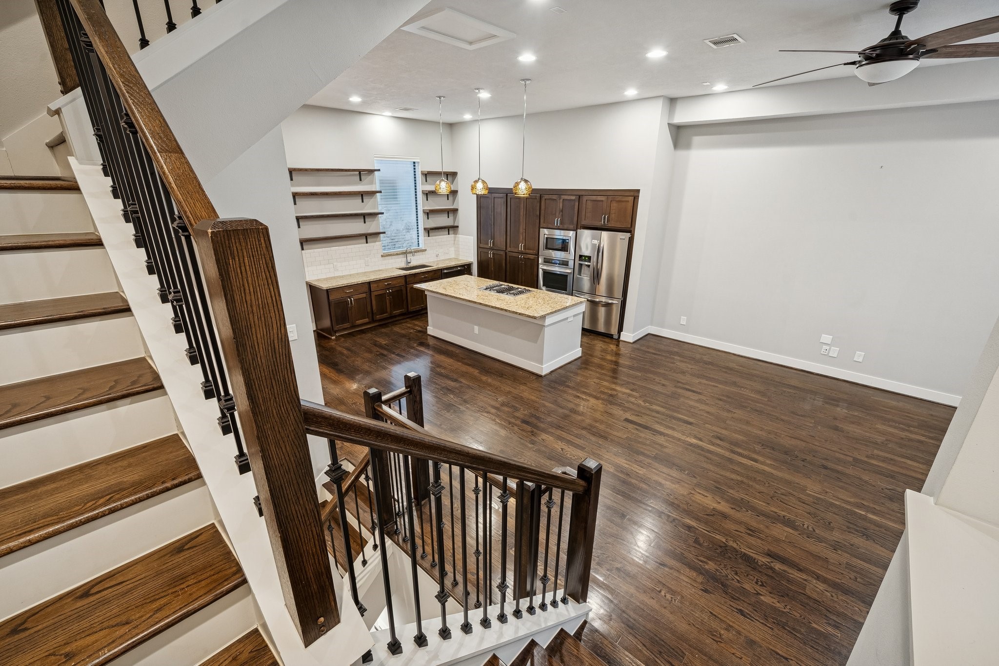2105 Mason Street Houston, TX 77006 - Photo 10 of 43 From the stair landing, you get a full look at how the kitchen sits at the heart of the main level with plenty of room around the island. Dark-stained hardwoods run continuously through the space, and recessed lighting keeps everything bright from corner to corner. The main level connects naturally between the stairs, kitchen, and living area for an easy day-to-day flow.
