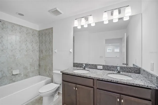 a bathroom with a granite countertop sink a toilet a mirror a bathtub and shower
