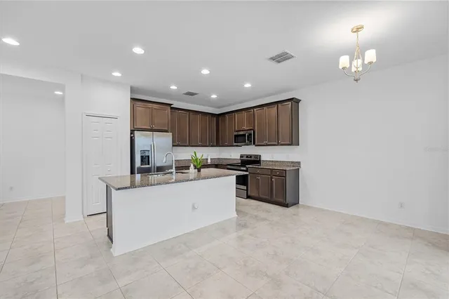 a kitchen with granite countertop a stove top oven a sink dishwasher a refrigerator and a dining table with wooden floor