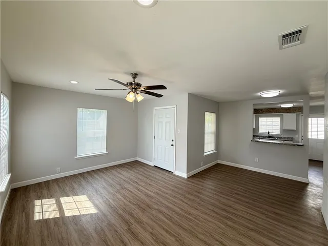 an empty room with wooden floor chandelier fan and windows