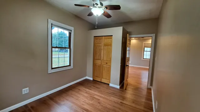 an empty room with wooden floor chandelier fan and windows