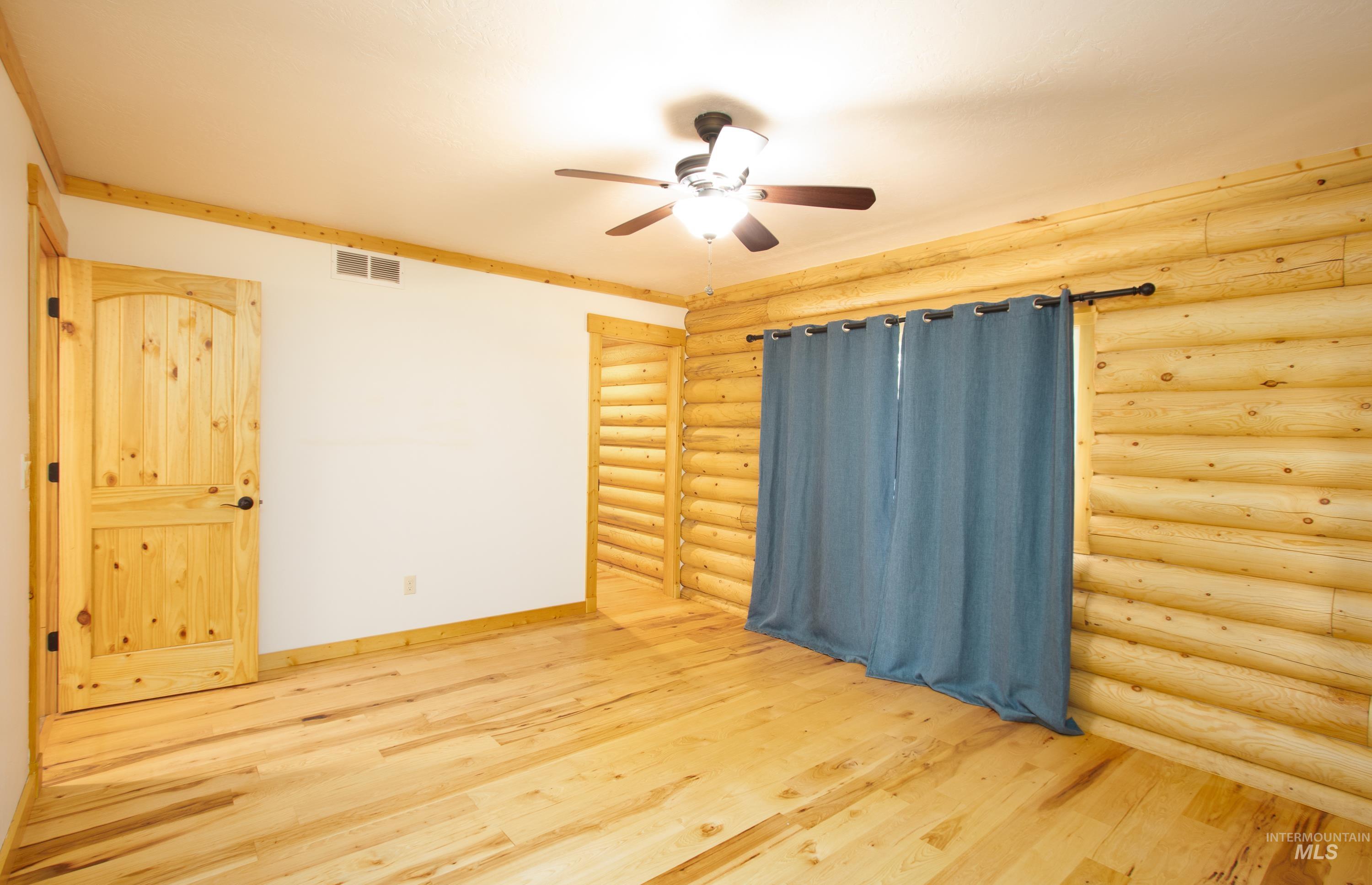1539 West Mountain Road Cascade, ID 83611 - Photo 11 of 33 Empty room featuring log walls, light wood-style flooring, and a ceiling fan