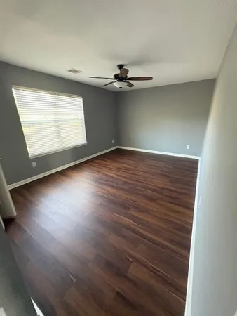 an empty room with wooden floor chandelier fan and windows