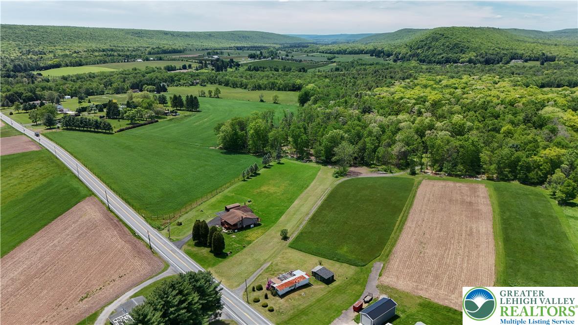 3551 Quakake Road Weatherly, PA 18255 - Photo 8 of 12 An aerial panorama reveals verdant fields, a winding road, and a cluster of homes nestled amidst rolling hills.