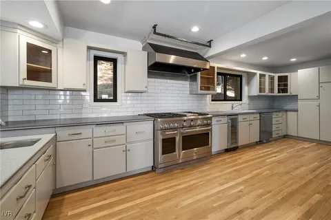 a kitchen with stainless steel appliances granite countertop a stove top oven a sink dishwasher and white cabinets with wooden floor