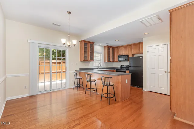 a kitchen with stainless steel appliances granite countertop a stove a refrigerator a sink a dining table and chairs with wooden floor