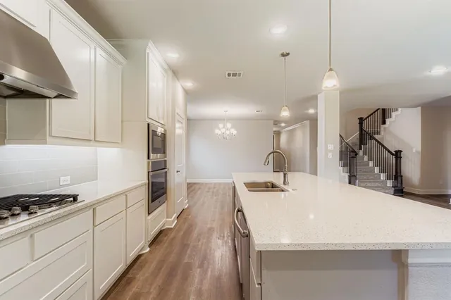 a view of an empty room with wooden floor and a kitchen