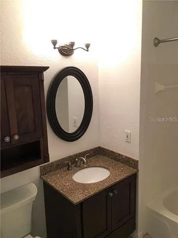 a bathroom with a granite countertop toilet a sink and a mirror
