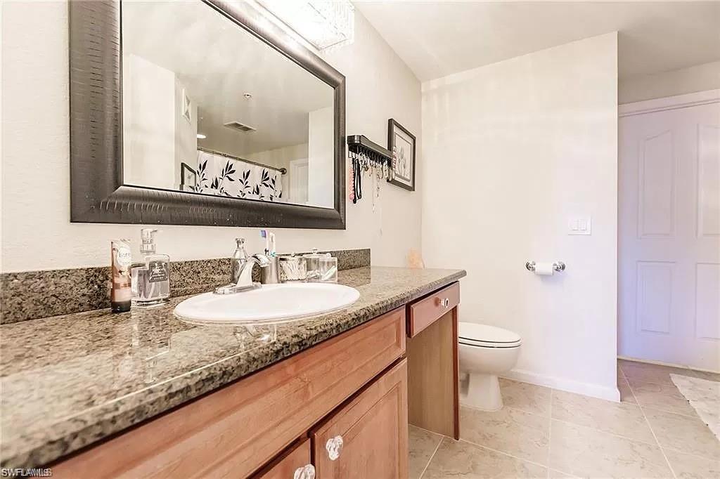 13010 Positano Circle, Unit 101 Naples, FL 34105 - Photo 25 of 29 a bathroom with a granite countertop sink mirror vanity and toilet