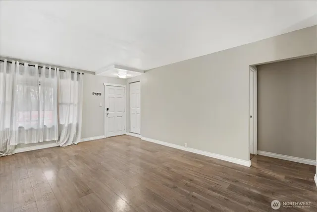 a view of an empty room with wooden floor and a window