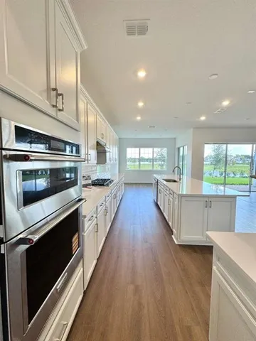 a kitchen with stainless steel appliances kitchen island granite countertop a stove a sink and white cabinets with wooden floor